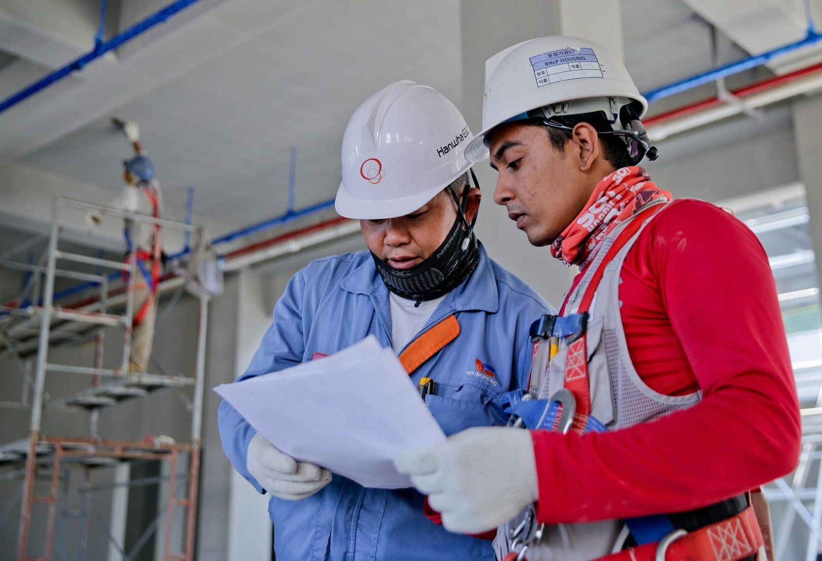 Two engineers in safety helmets reviewing construction plans at a worksite.