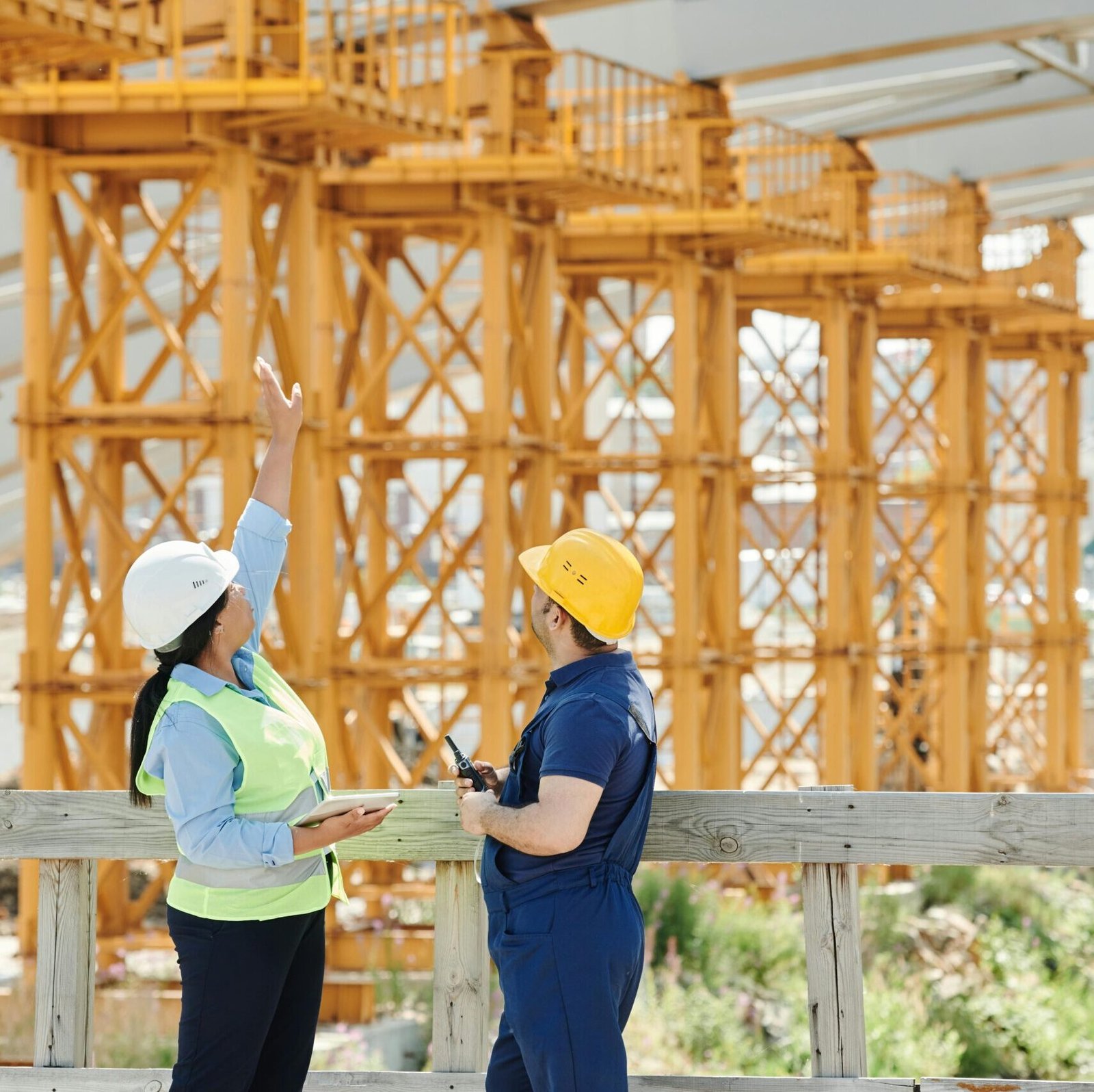 Two engineers in hardhats discuss projects at a busy construction site.